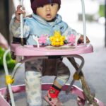 Un bébé mignon joue dans un trotteur rose, bien emmitouflé à l'intérieur.