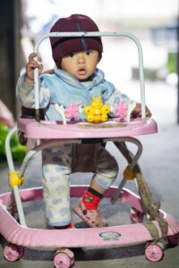 Un bébé mignon joue dans un trotteur rose, bien emmitouflé à l'intérieur.