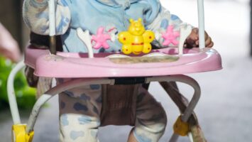 Un bébé mignon joue dans un trotteur rose, bien emmitouflé à l'intérieur.