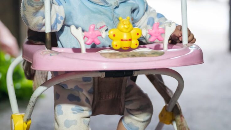 Un bébé mignon joue dans un trotteur rose, bien emmitouflé à l'intérieur.