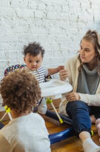 Une mère joue avec ses deux jeunes enfants dans un salon chaleureux, montrant ainsi le lien familial.
